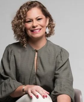 Retrato de Jordana Marinho sorrindo, com cabelos cacheados e blusa verde-oliva.