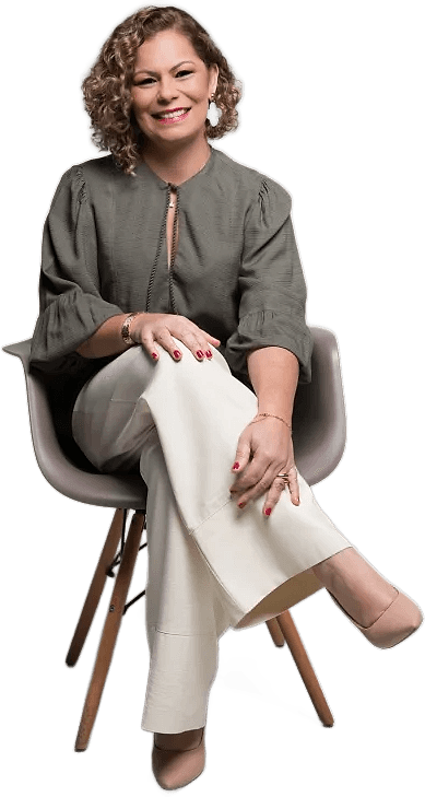 Jordana Marinho sorrindo, sentada numa cadeira, de blusa verde-oliva e calça clara.